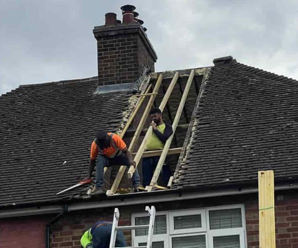 This is a photo of a roof repair being carried out. A section of the roof has been stripped and two roofers are replacing the rafters. Works being carried out by NGF Roofing Brixworth